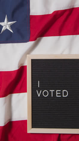 Vertical-Video-Of-Sign-Reading-I-Voted-Lying-On-US-Stars-And-Stripes-Flag-For-American-Election-2024-3